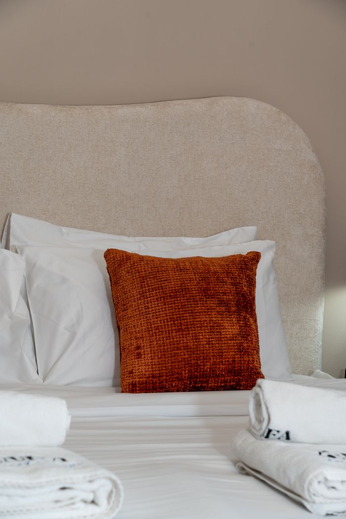 Elegant bed with vibrant orange cushion and fresh towels in a Dubai setting.